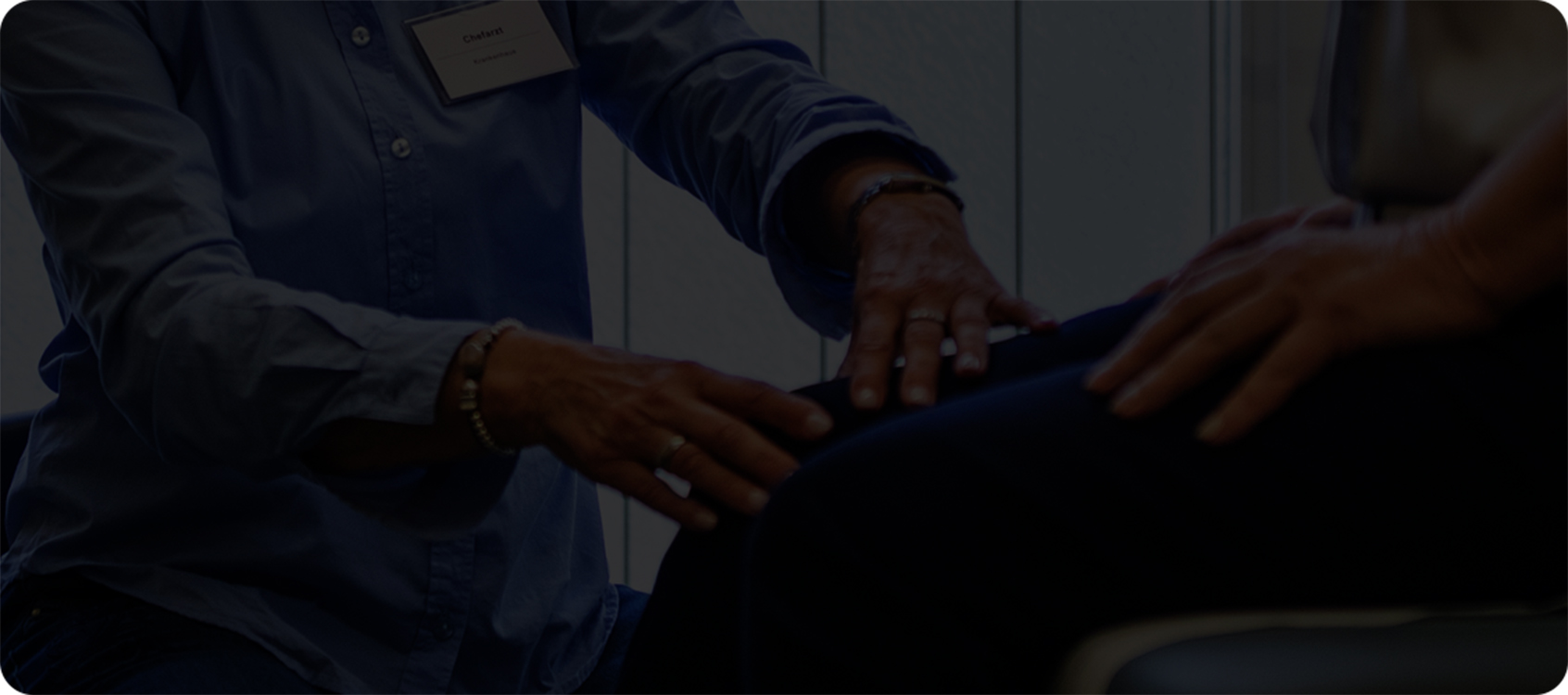 close up photograph of a patient sitting on a table and a healthcare professional touching the patient’s right knee
